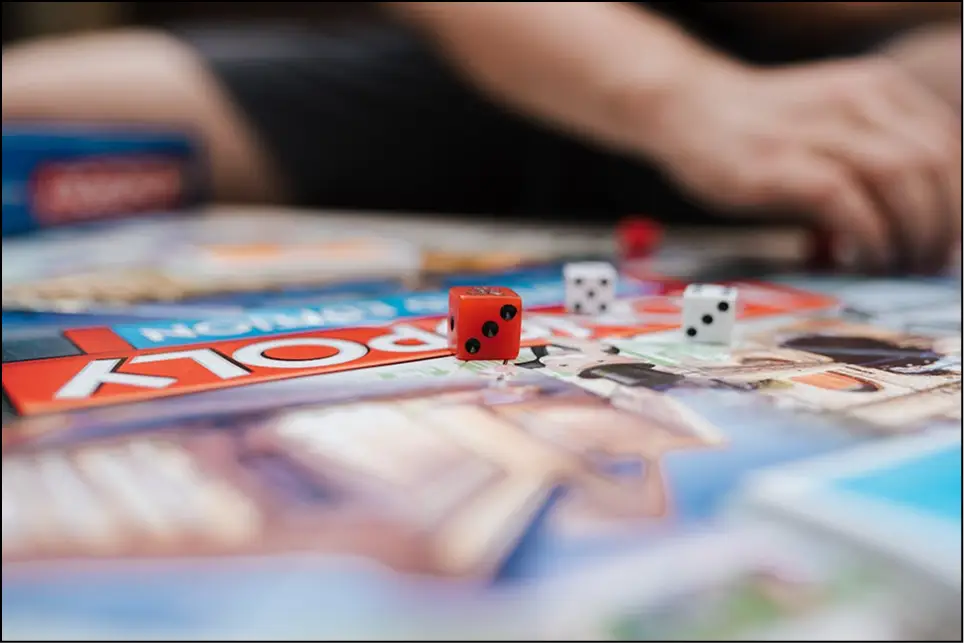 Zbliżenie na rzucanie kostką i grę Monopoly podczas rodzinnej zabawy, kostki i kolorowe elementy gry na stole.