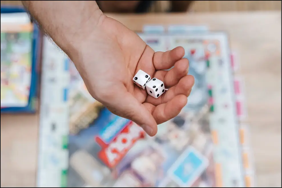 Zbliżenie na rzucanie kostką i grę Monopoly podczas rodzinnej zabawy, kostki i kolorowe elementy gry na stole.